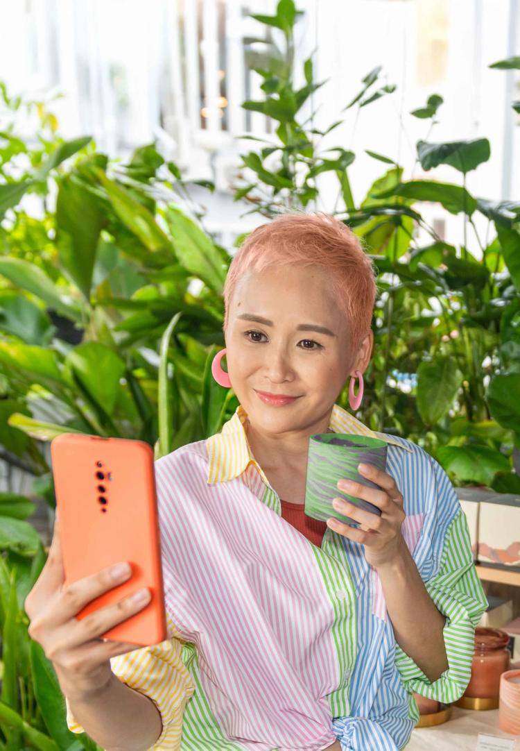 A young Asian woman in a store takes a selfie as she holds a decorated pot.