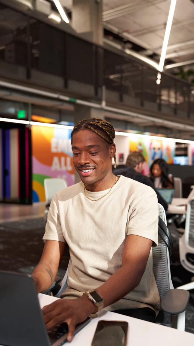 A young Black TikTok employee smiles as he works at his computer.