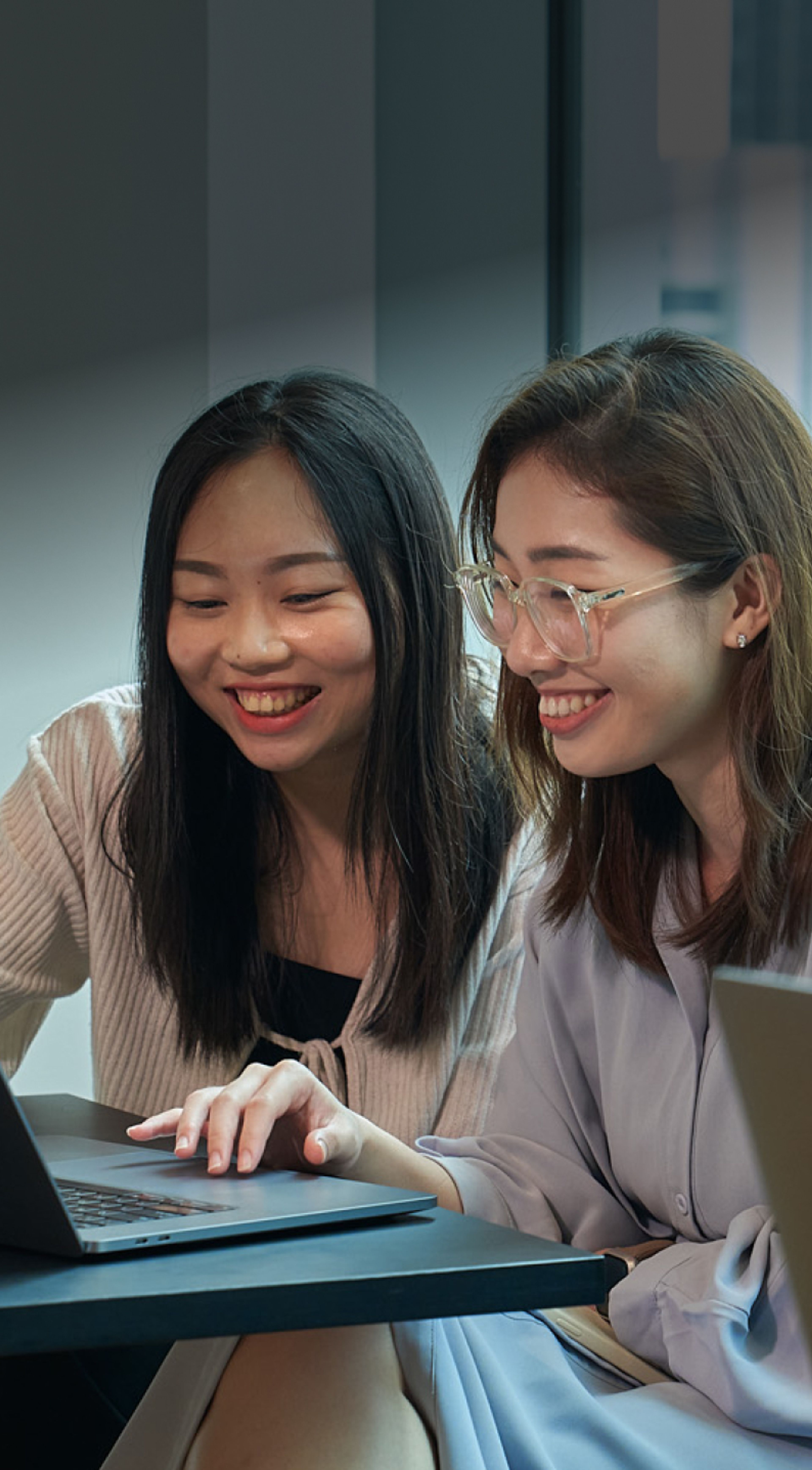 Two TikTok female employees wearing office attire smile as they look at a mobile phone screen.