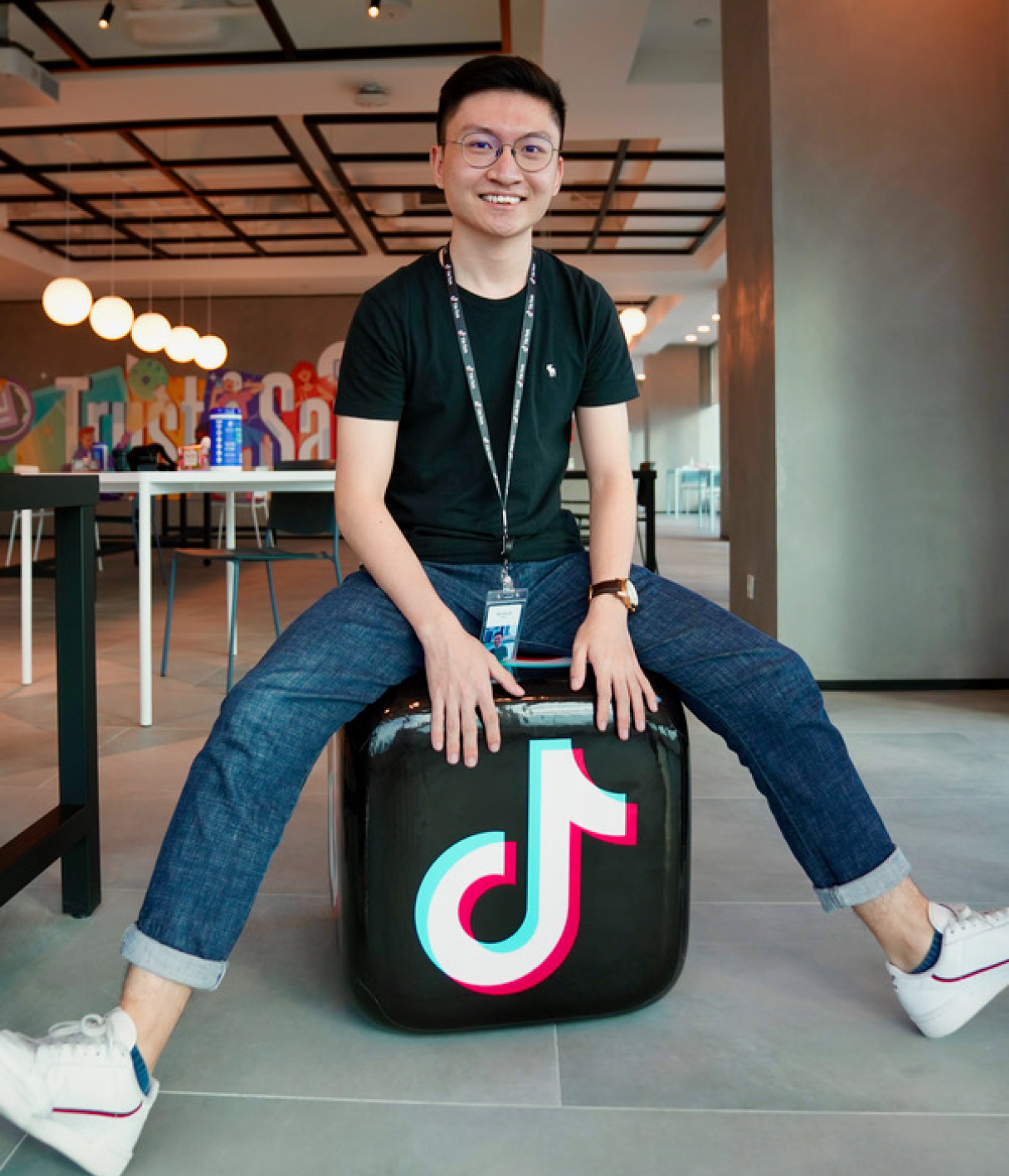 An young Asian male TikTok employee sits on a plastic cube that has the TikTok music note logo on it.