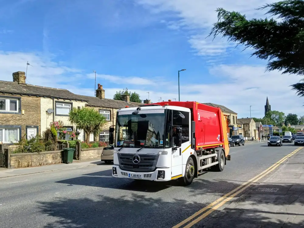 A waste collection lorry that's red and white driving down a UK street