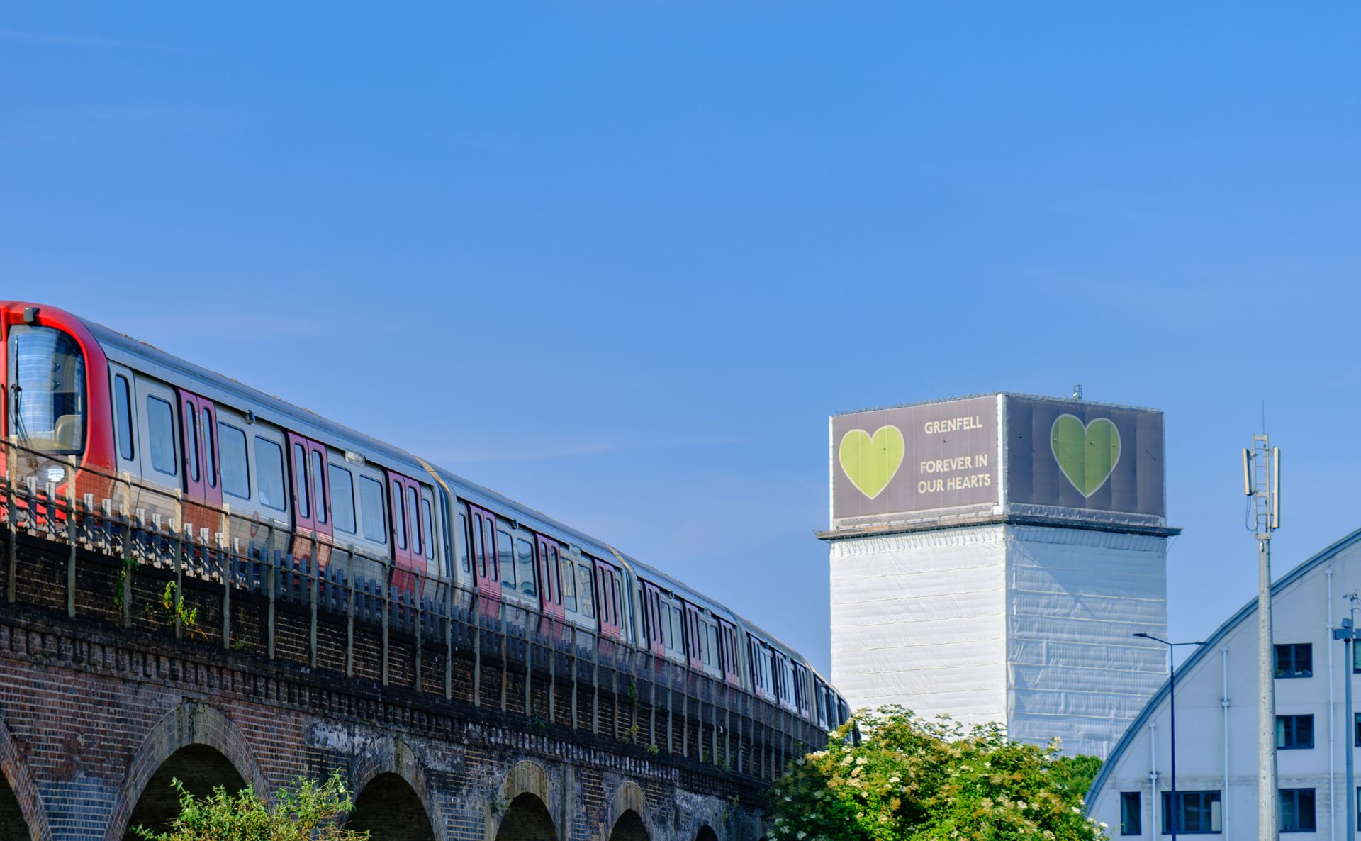 tube going overground with Grenfell tower covered in it's memorial cladding in the background.
