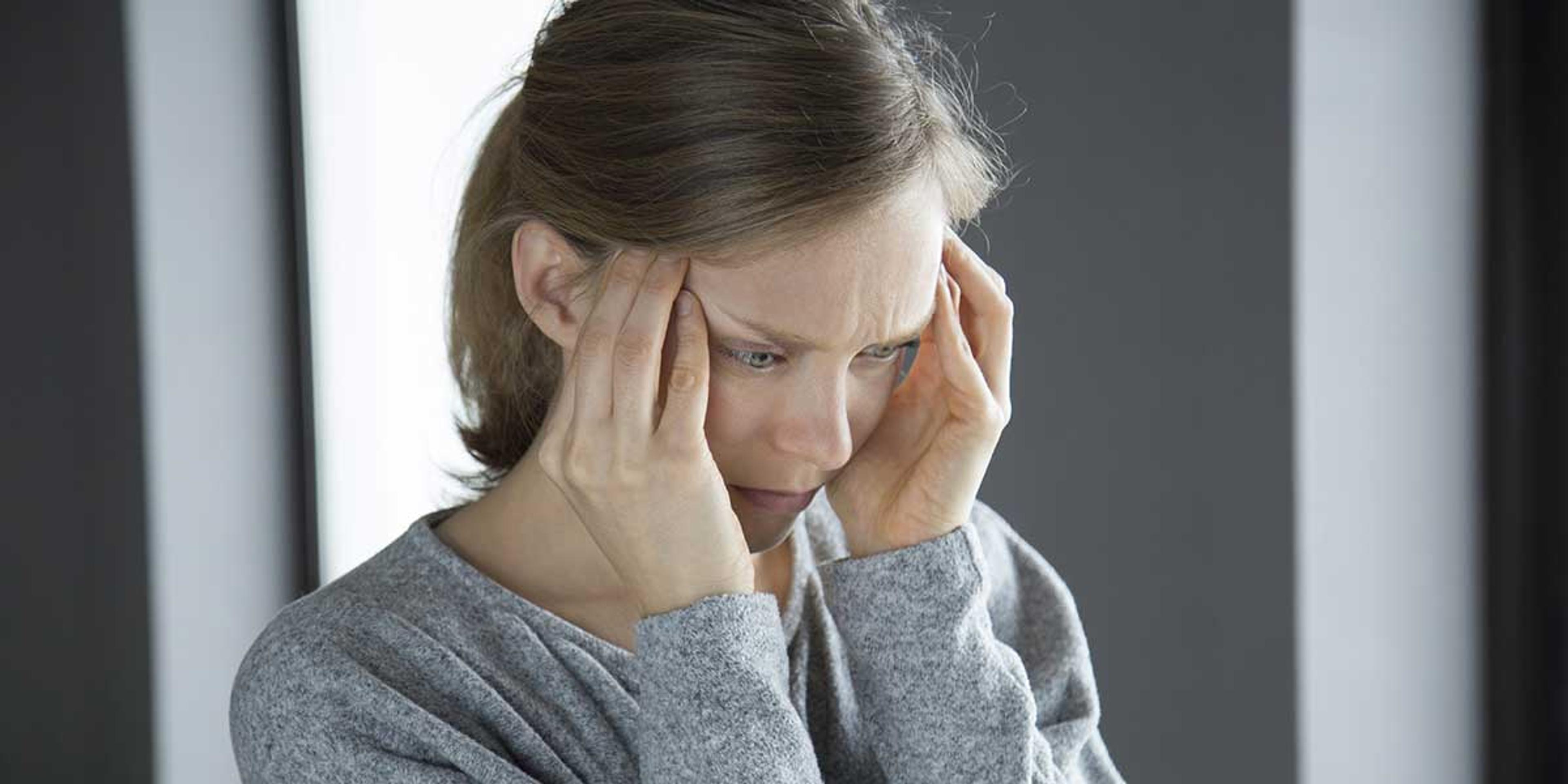 Woman holding her temples in pain, illustrating the symptoms and differences between cervicogenic headaches and severe migraine conditions.