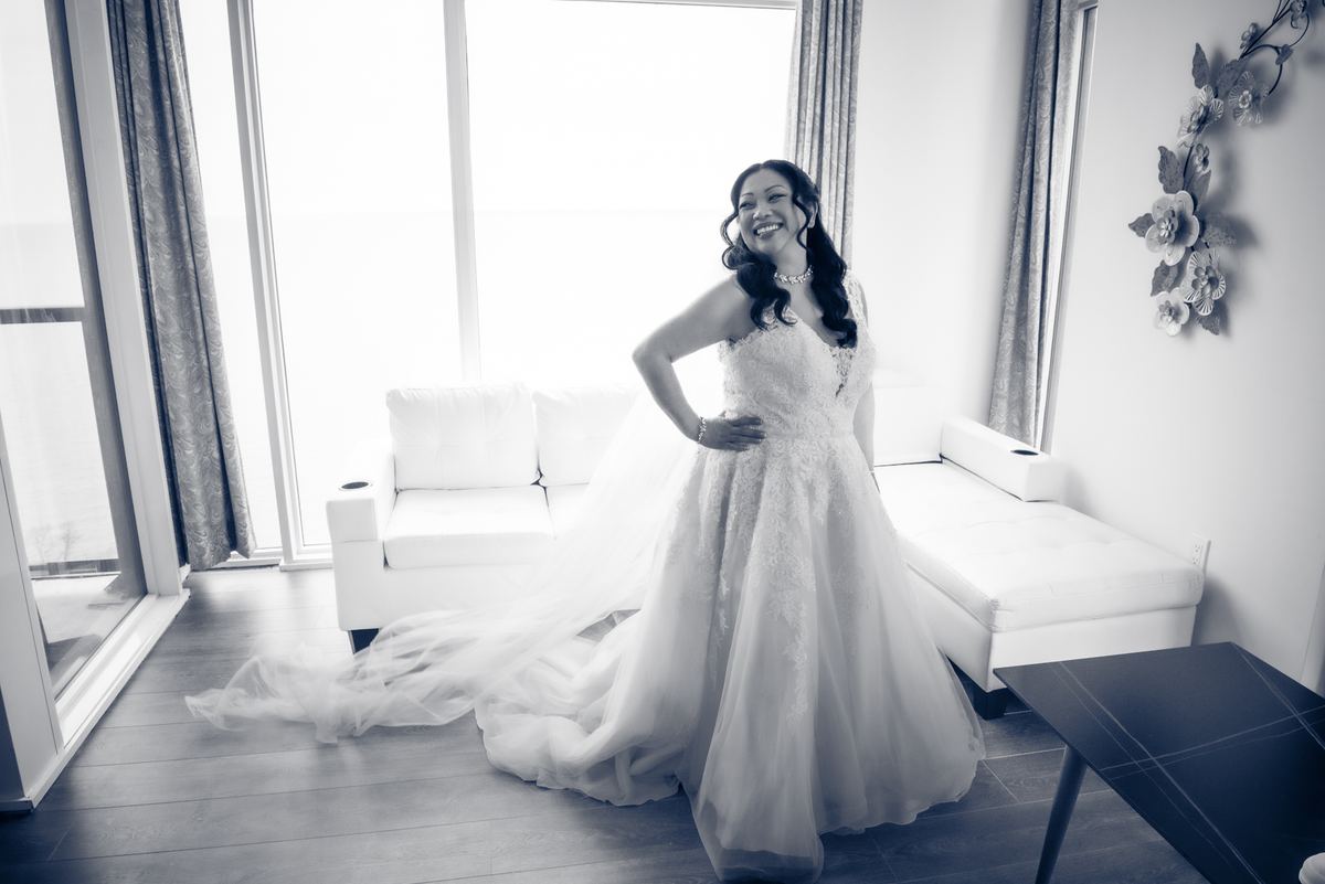 A laughing bride in her wedding gown poses joyfully in a modern, sunlit room with white furnishings.