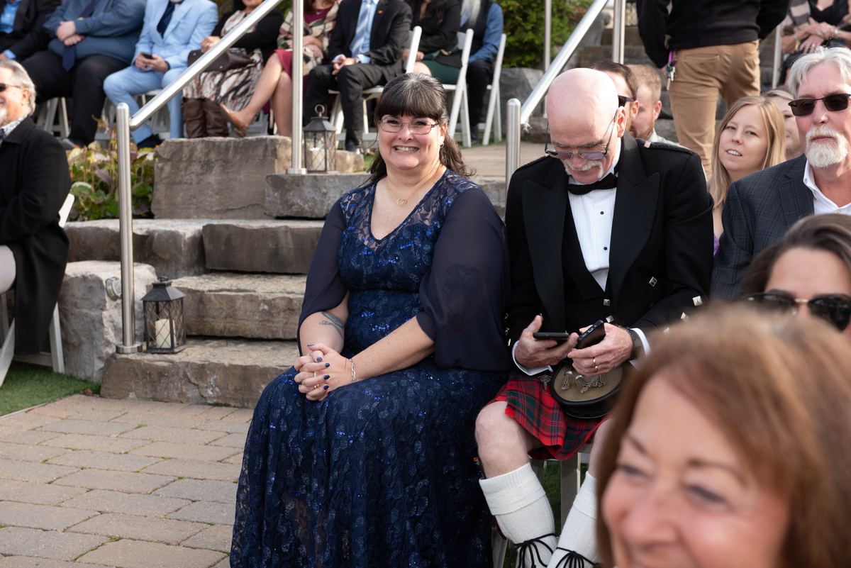 A smiling bride in a blue lace gown and her groom in a kilt exchange glances during their wedding ceremony.
