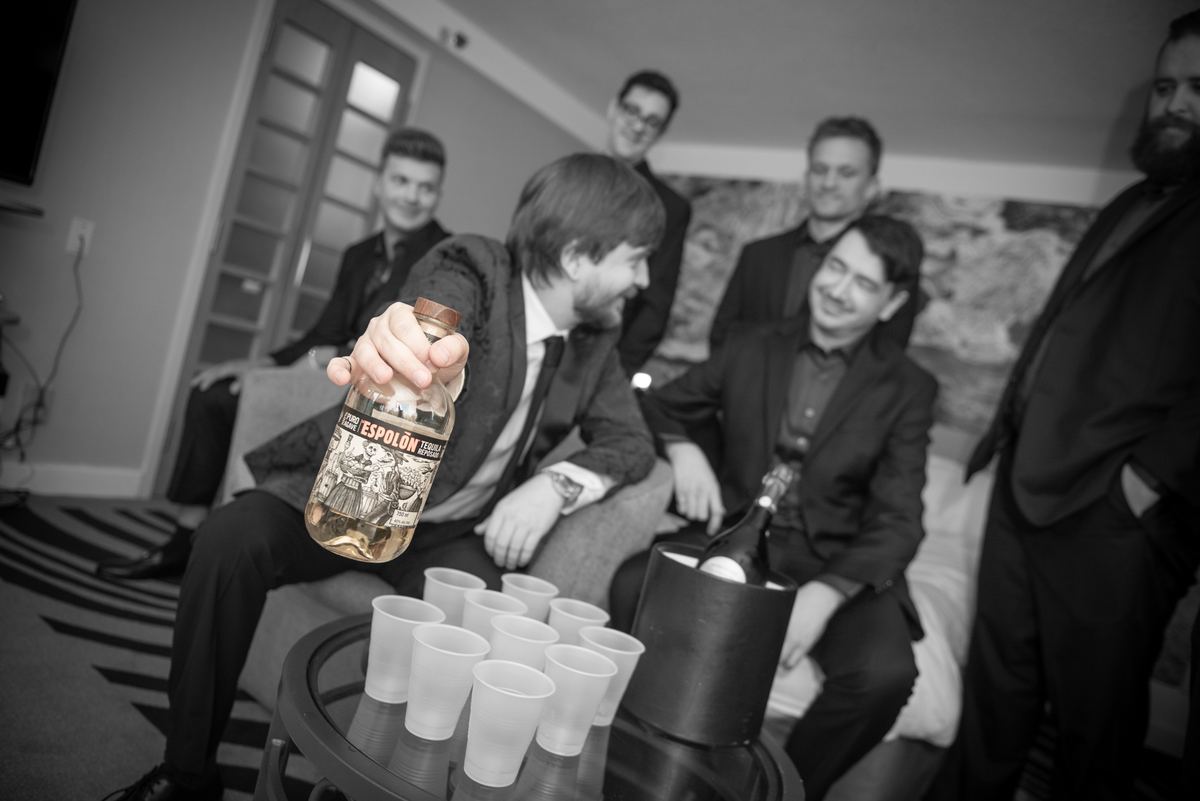 Men in suits laughing and playing beer pong, one holding up a bottle of Espolón tequila, creating a celebratory atmosphere.