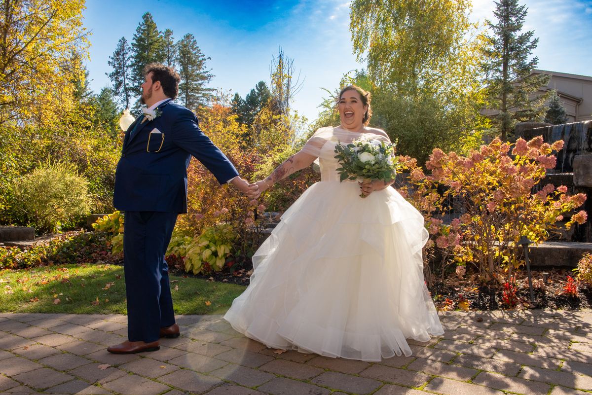 A joyful bride laughs as she spins with her groom in a sun-drenched garden, their hands clasped and eyes locked.