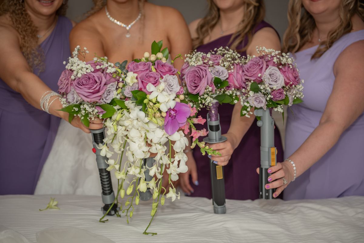 Bridesmaids in lavender gowns hold floral bouquets mounted on lightsaber hilts, exuding joy and camaraderie.