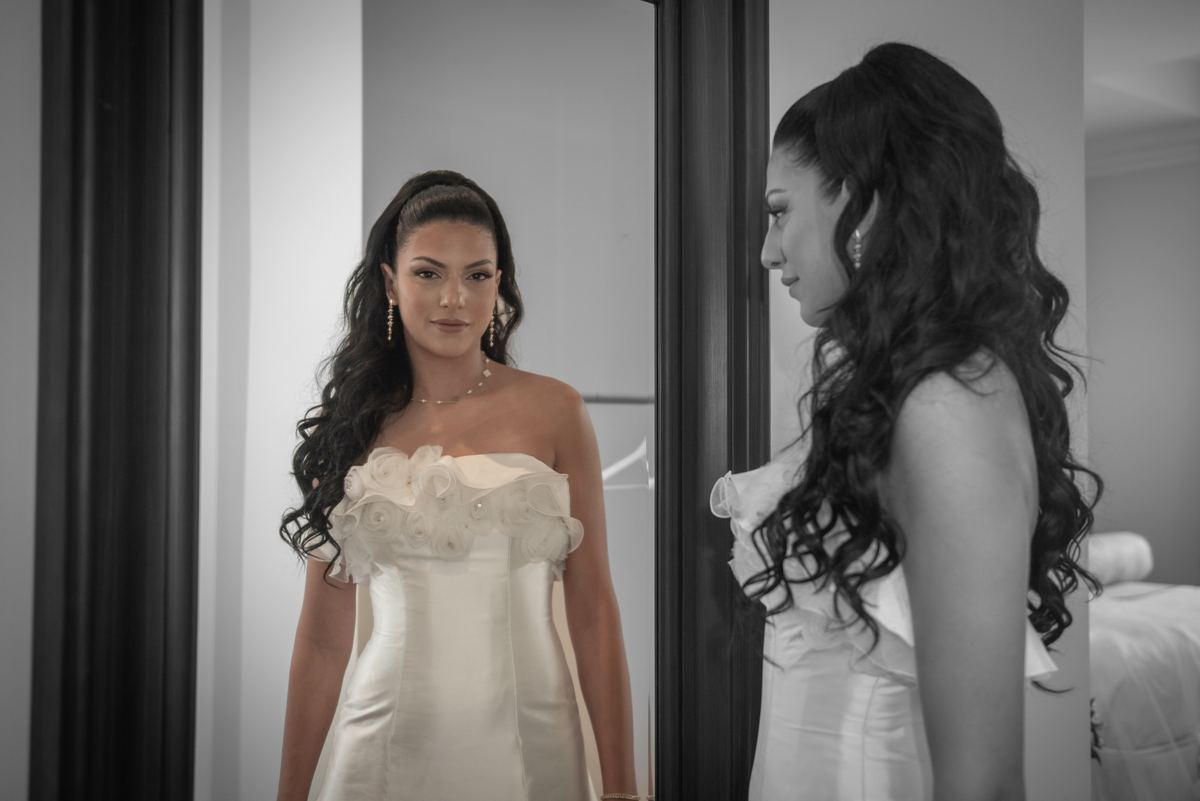 A bride looks at her reflection in a mirror as she prepares for her wedding, emphasizing the elegance of her gown.