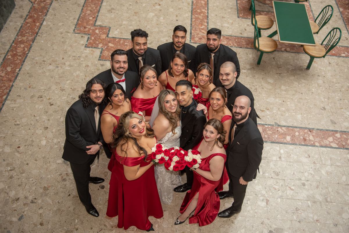 Cassandra and Brandon stand at the center of an overhead group portrait, surrounded by their wedding party in formal attire.