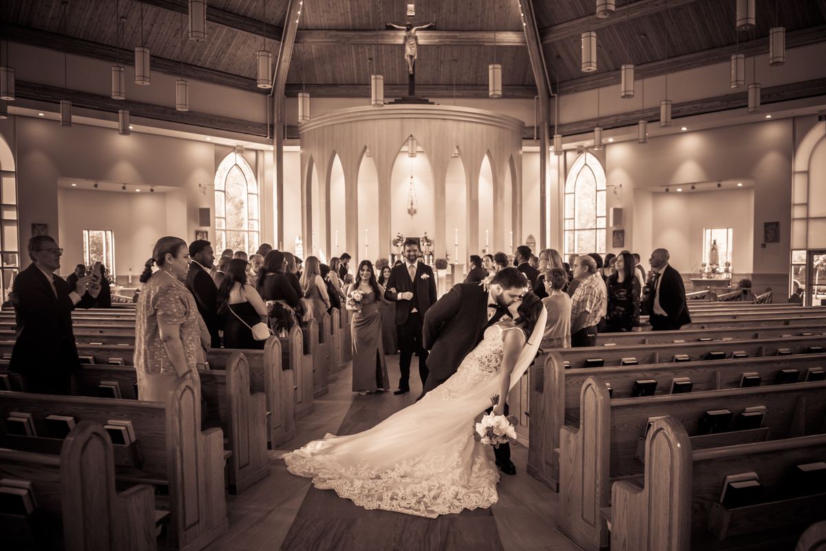 A bride and groom embrace as they walk down the aisle of a church, surrounded by guests in wooden pews.