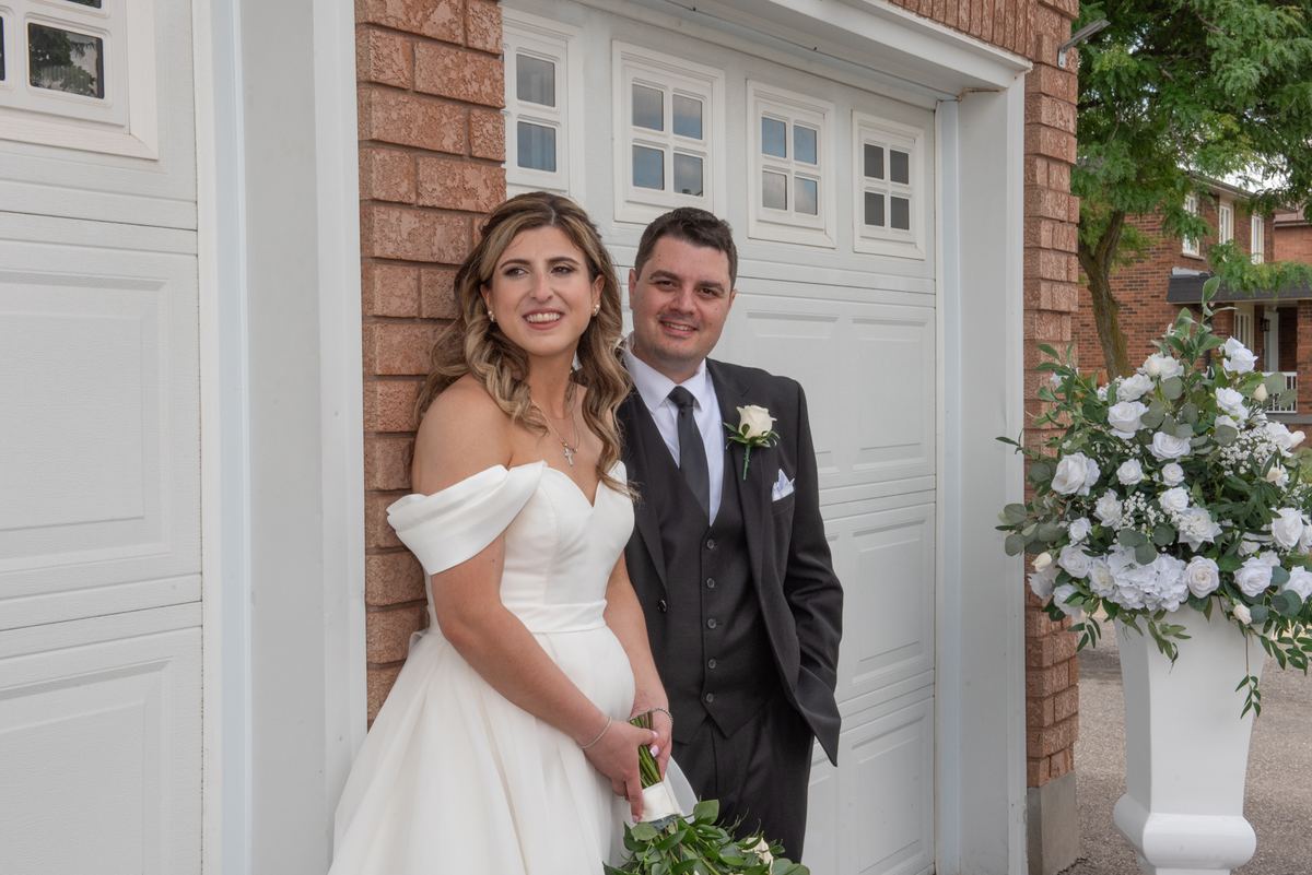 Vittoria and Vince smile warmly for the camera, standing beside a white garage door framed by brickwork.