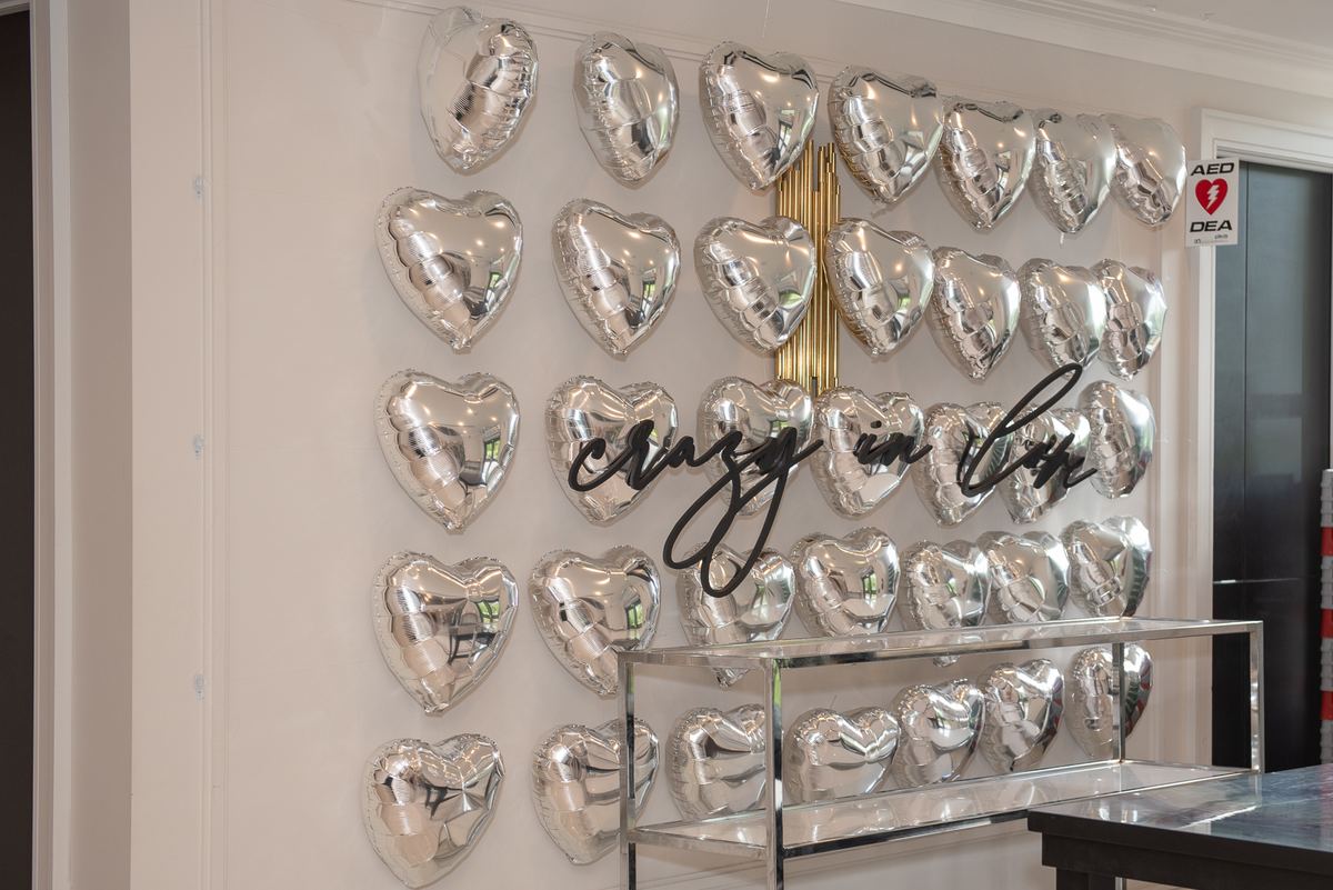 A wall covered in silver heart-shaped balloons arranged in a grid with black script reading 'crazy in love' above them.