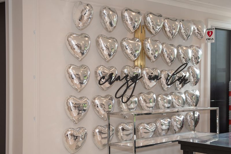 A wall covered in silver heart-shaped balloons arranged in a grid with black script reading 'crazy in love' above them.