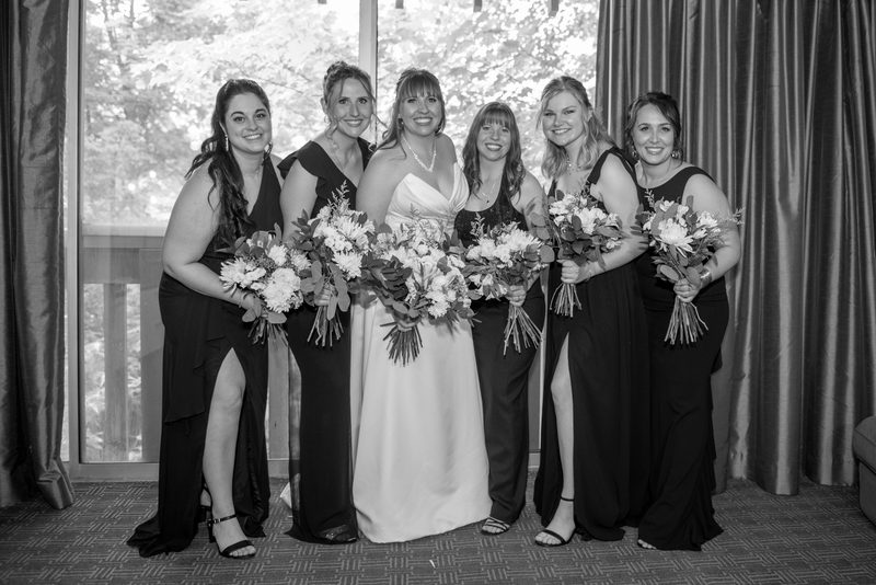 A bride and her bridesmaids pose together near a window, illuminated by natural light filtering through the curtain.