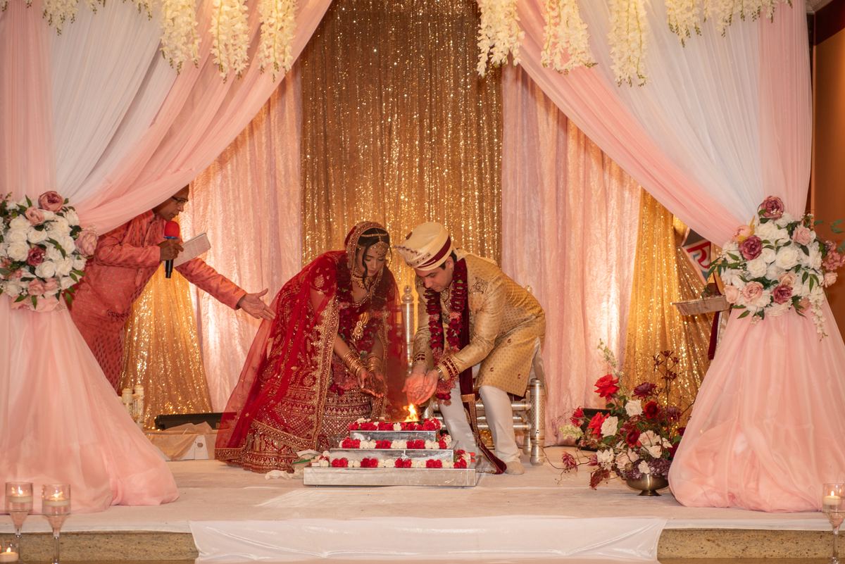 A bride and groom light a ceremonial candle on a cake, framed by floral arrangements and soft lighting.