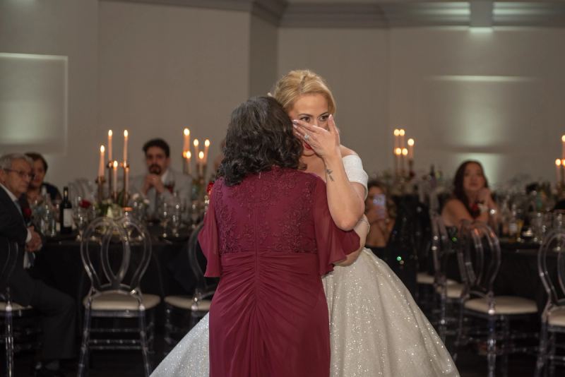 A bride in a sparkling gown embraces her emotional a family member, who covers her face with her hand at the reception.