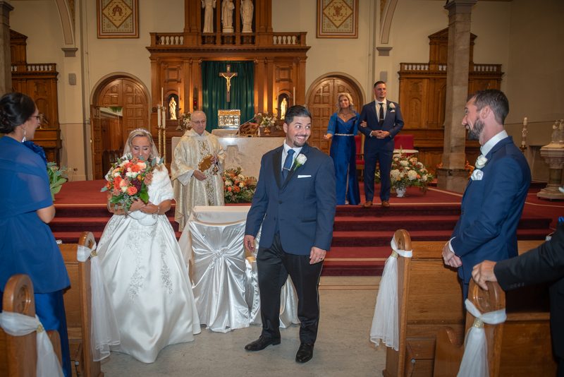 Bride and groom walk down the aisle toward an ornate altar during a wedding ceremony in a warmly lit church.