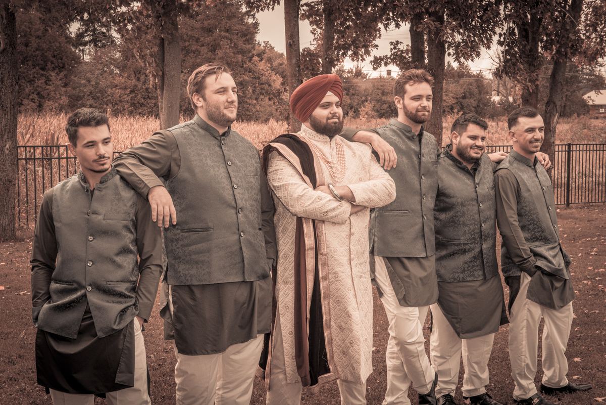 A groom and his groomsmen pose in a wooded setting, dressed in coordinated attire on an overcast day.