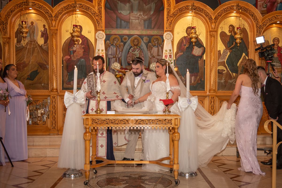 A couple exchanges vows at an ornate altar with clergy and guests, illuminated by warm light and golden icons.