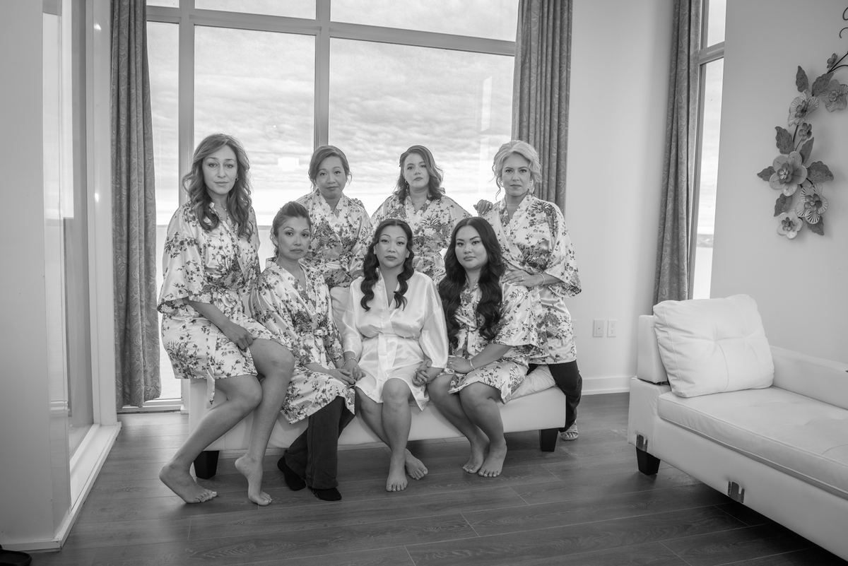 Seven bridesmaids in matching robes pose indoors during wedding preparations, with natural light streaming through windows.