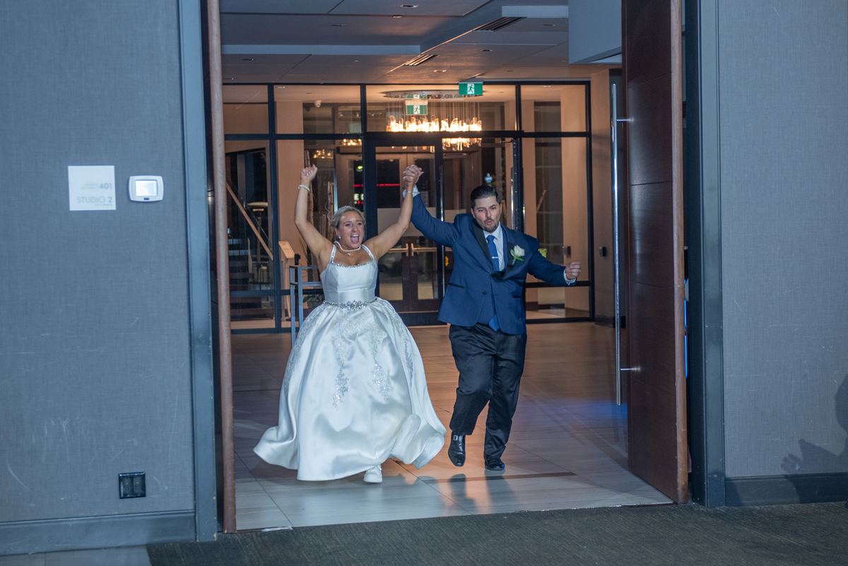 Vanessa and Kevin burst through a doorway in joyful celebration, their arms raised as they exit an indoor space.