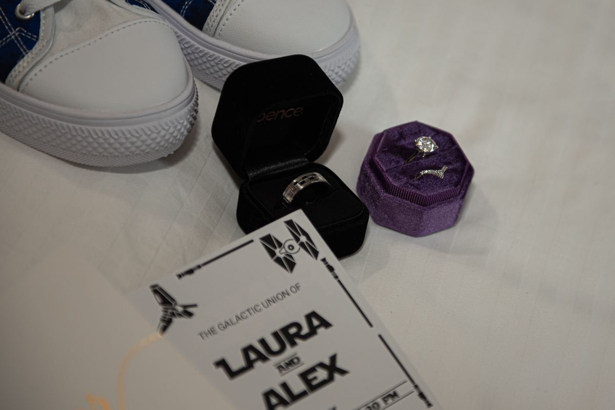 A wedding invitation and two rings in themed boxes next to white sneakers, suggesting a casual celebration.