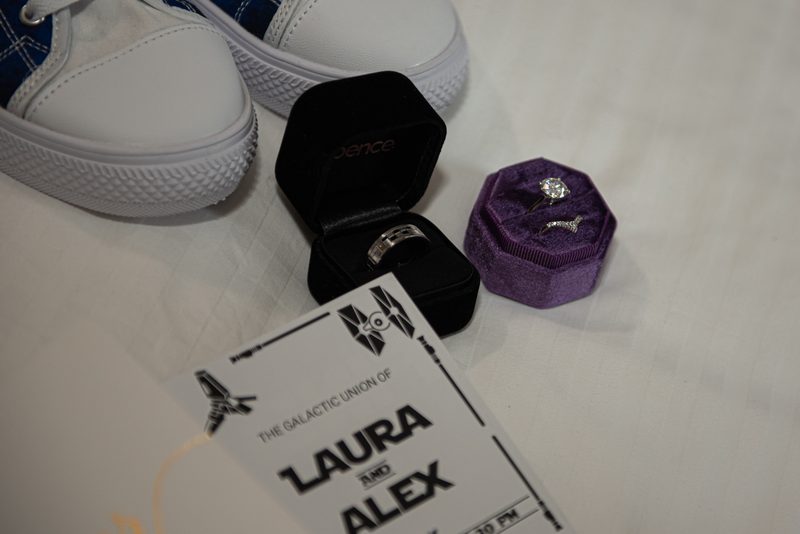 A wedding invitation and two rings in themed boxes next to white sneakers, suggesting a casual celebration.