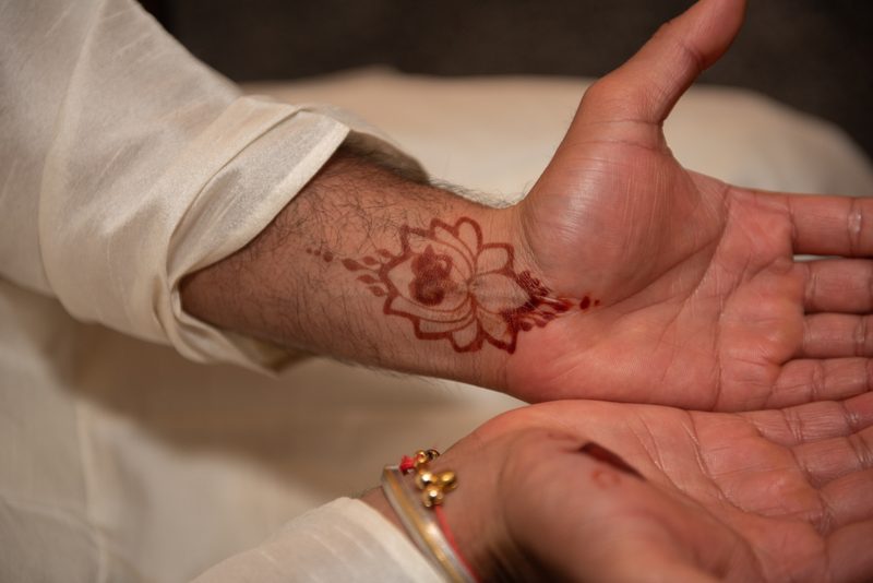 A person shows off intricate henna designs on their wrist and palm, adorned with traditional bangles.