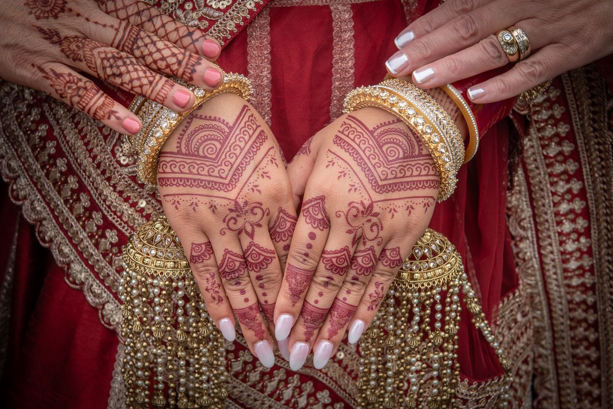 Two hands decorated with henna and jewelry resting against an embroidered garment during a celebration.