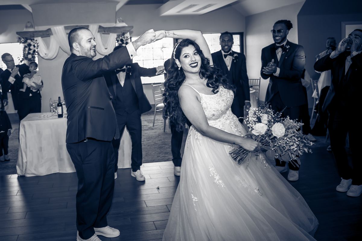 A bride and groom dance joyfully in the center of a wedding reception surrounded by clapping guests.