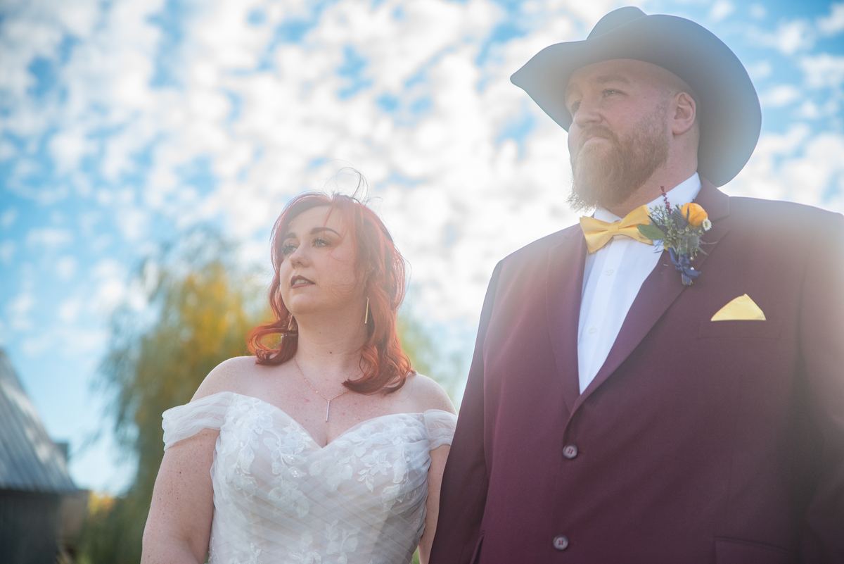 Bride and groom stand outdoors in warm sunlight, gazing upward with serene expressions during their wedding day.