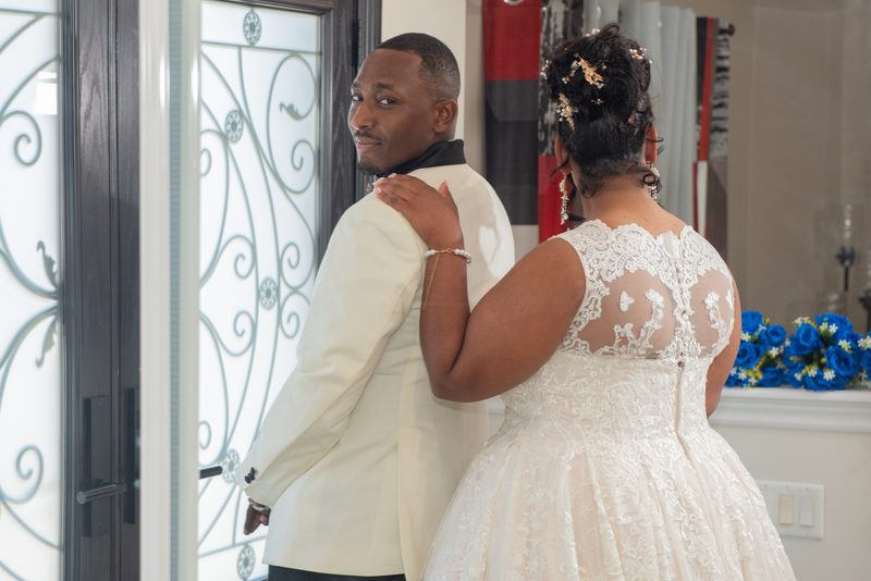 A bride and groom stand back-to-back in an indoor space with ornate glass doors and blue floral arrangements.