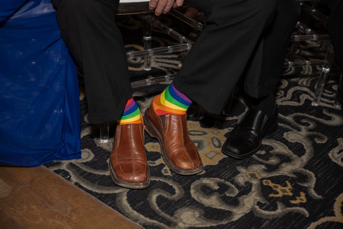 Three people seated indoors with focus on their feet and legs, one wearing bright rainbow-striped socks.
