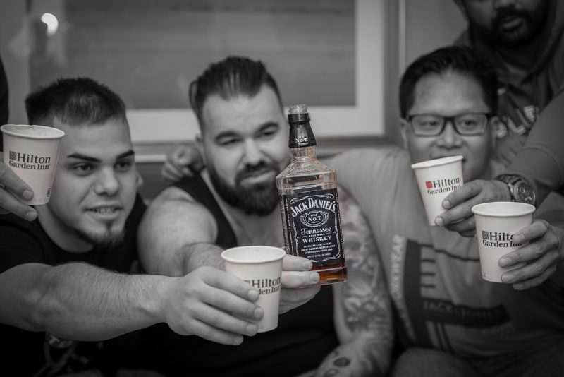 Men in casual attire raising Hilton Garden Inn cups and toasting with Jack Daniel’s, creating a warm atmosphere.