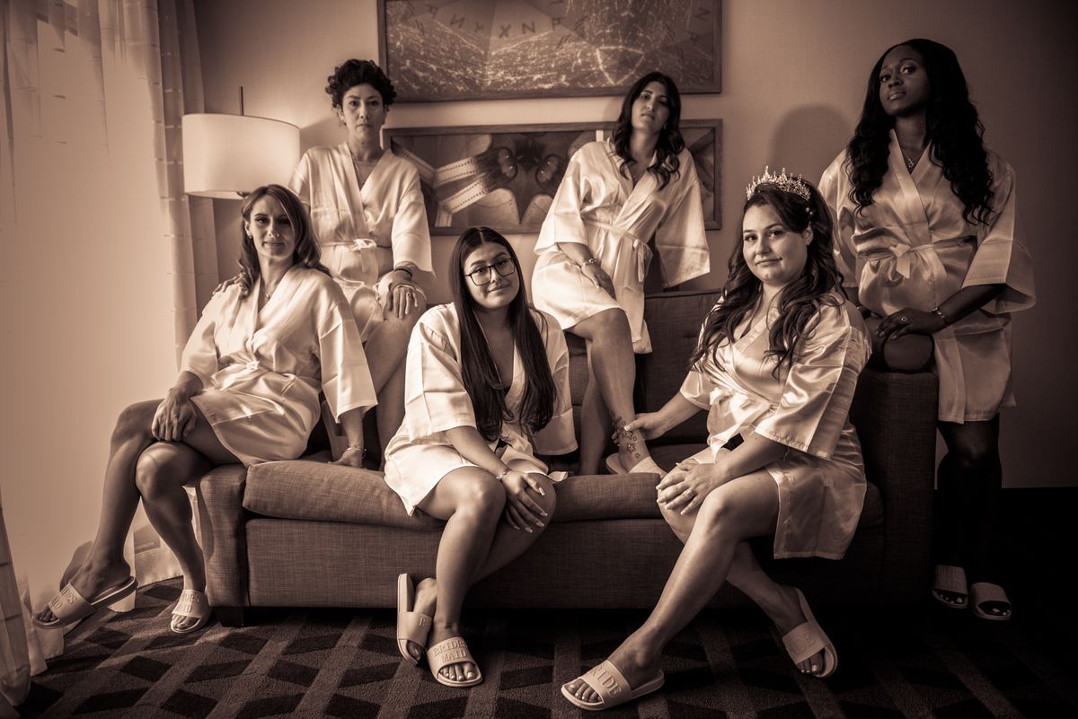 A sepia-toned photograph captures Gabriela and her bridal party in a hotel room, posing on and around a sofa.