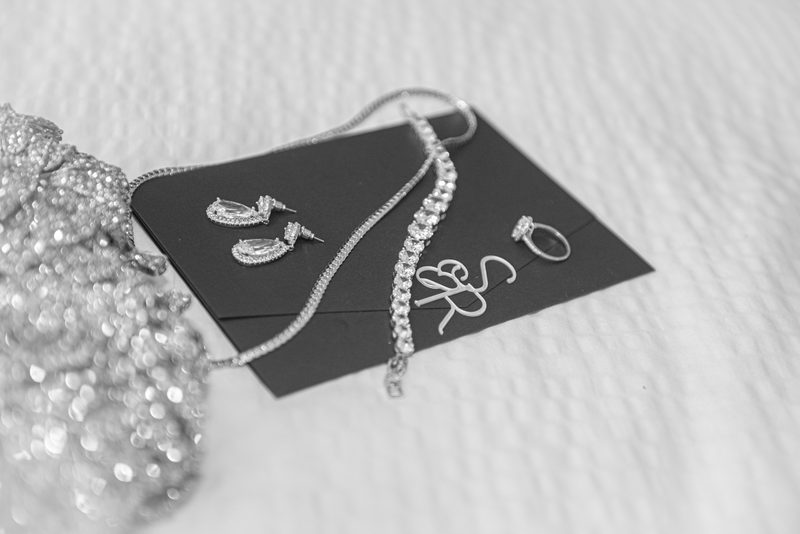 Bridal jewelry including earrings, necklace, bracelet, and ring laid out on a dark card, sparkling under soft light.