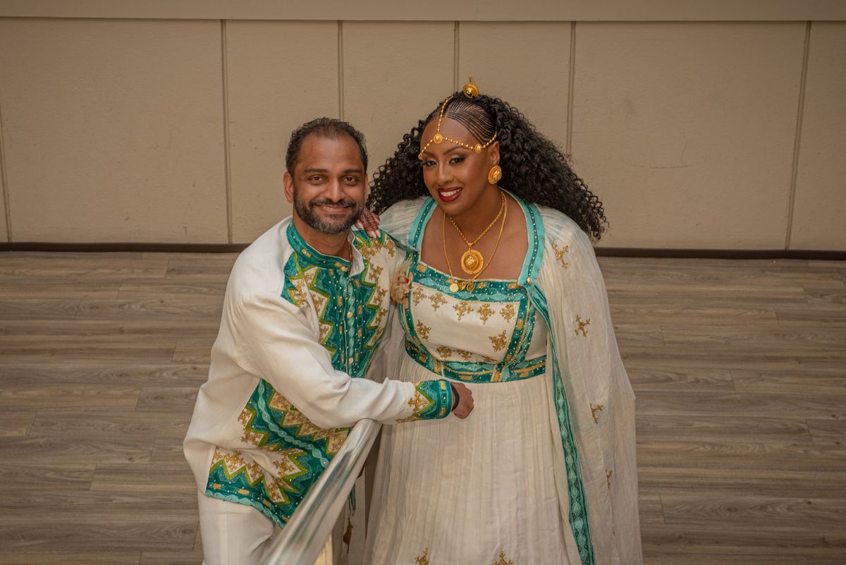 Salem and Shannon, dressed in ornate traditional attire, pose closely together with smiles in a warmly lit indoor space.