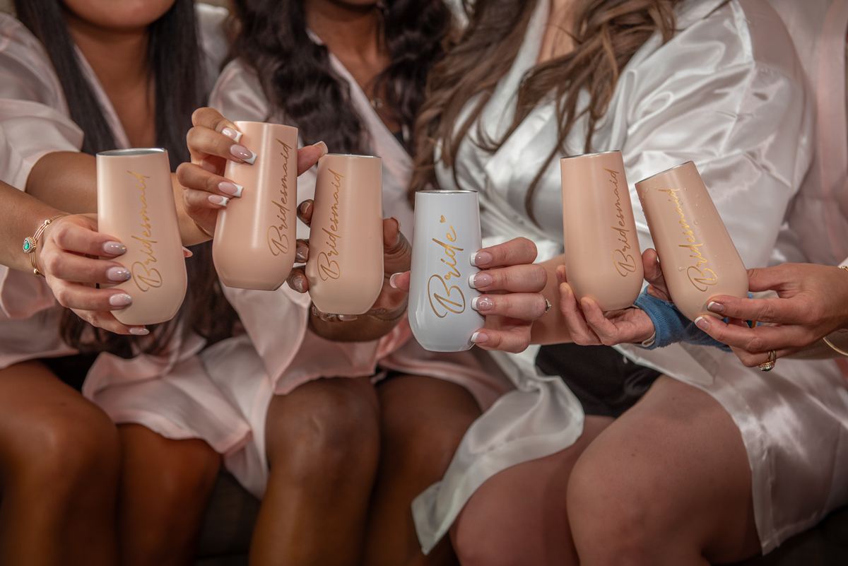 A bride and her bridesmaids gather closely, holding personalized champagne flutes in a celebratory toast.