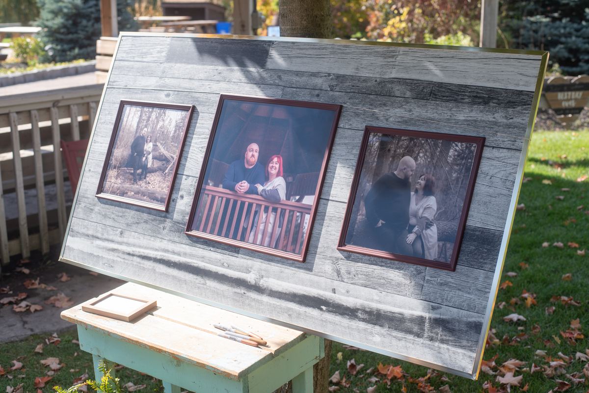 Three framed portraits of couples displayed on a rustic wooden board in a grassy yard with autumn leaves.