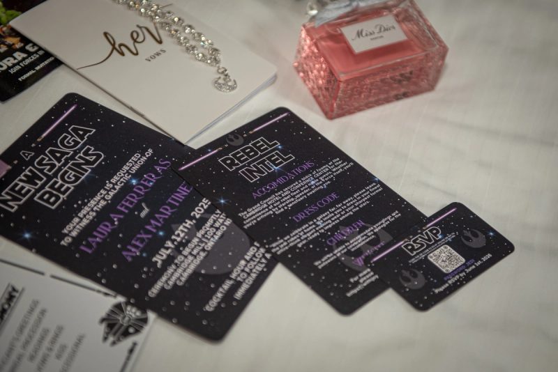 Star Wars wedding invitations, a pink perfume bottle, and a sparkling bracelet are arranged on a white surface.