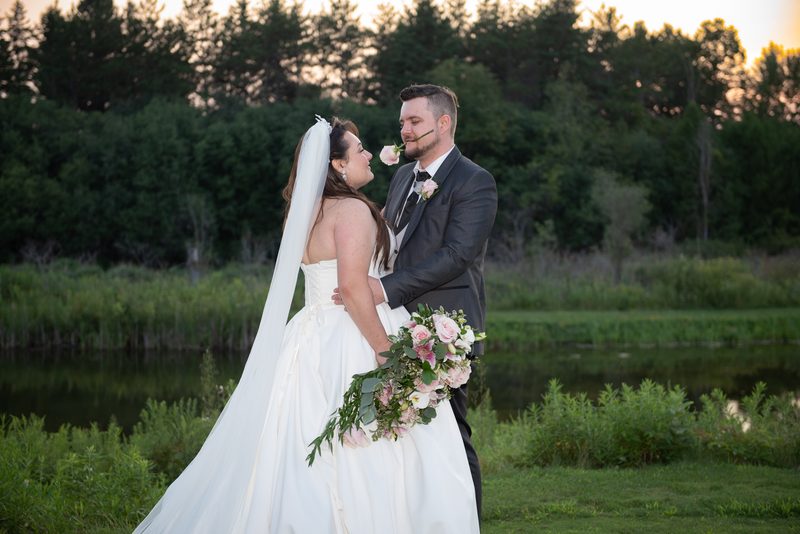 Gabriela and Bryce share a tender moment beside a pond at sunset, their faces illuminated by the soft golden light.