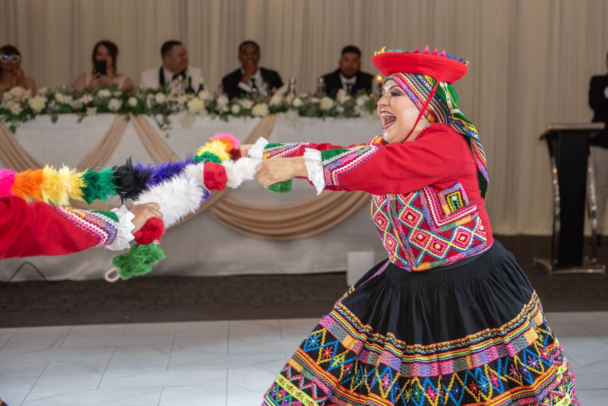 A dancer in vibrant traditional attire pulls a colorful feathered rope with a partner during a celebration.