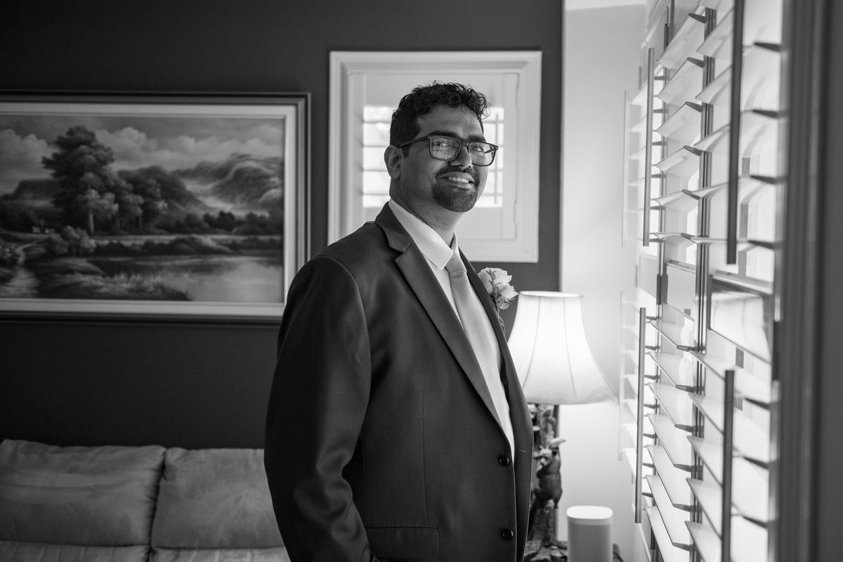 Stefan, dressed in a suit and boutonnière, stands indoors with a warm smile, looking toward the right.