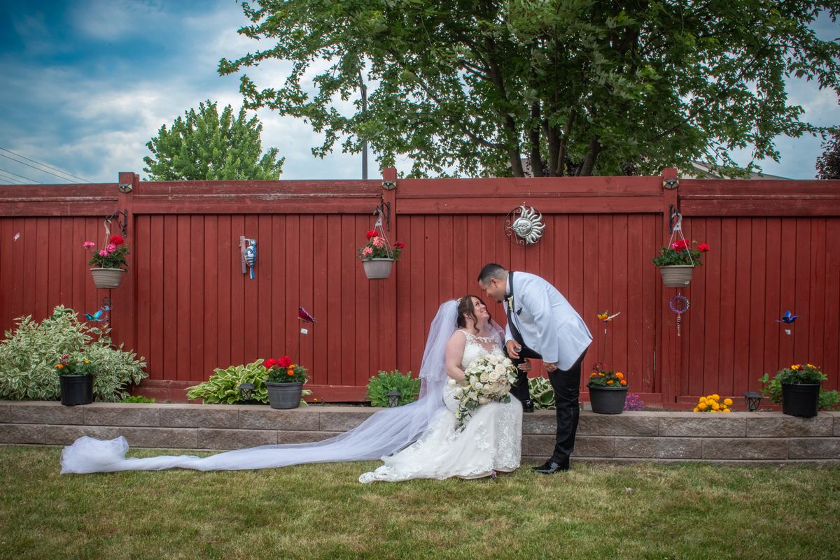 A bride and groom share an intimate moment outdoors, with the groom kneeling beside her as they gaze lovingly at each other.