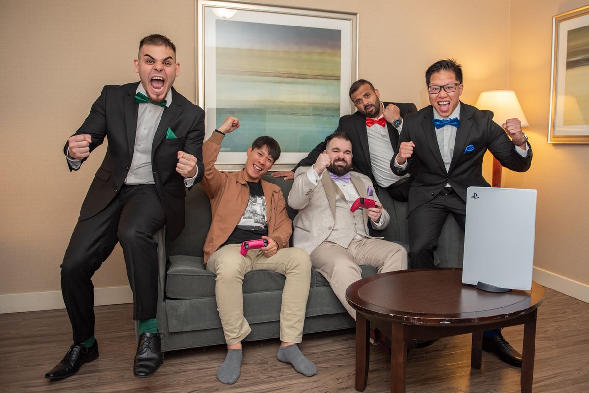Five men in suits celebrate a video game victory with raised fists and grins around a PlayStation 5.