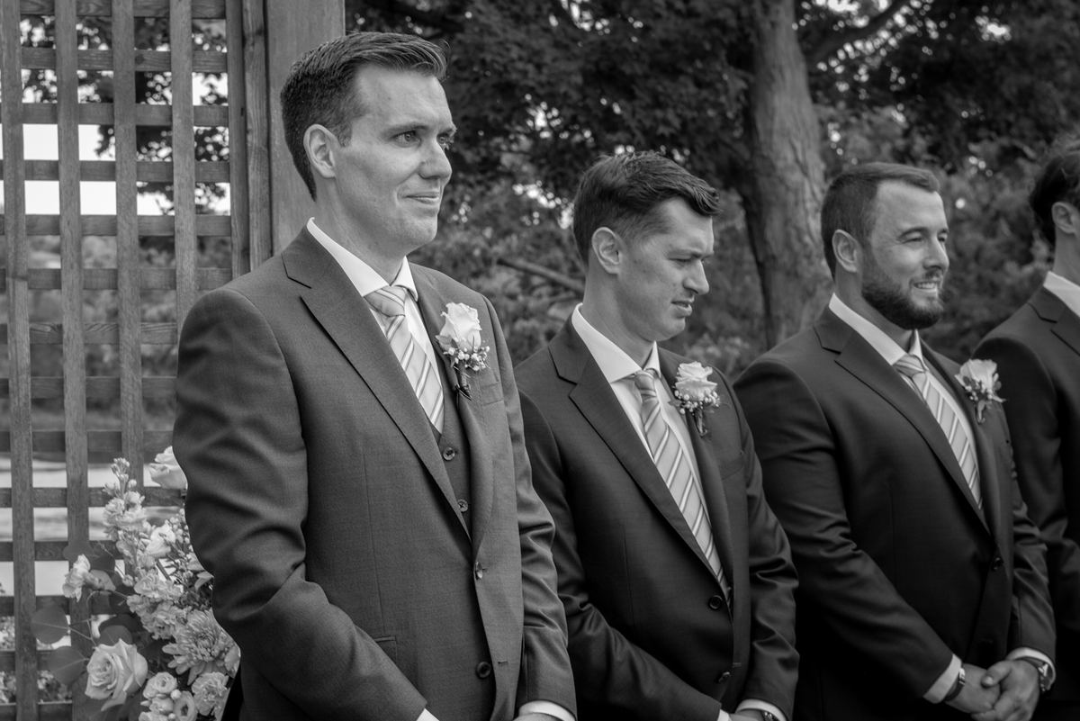 Groomsmen stand in line, their expressions ranging from hopeful smiles to quiet concentration on an overcast day.