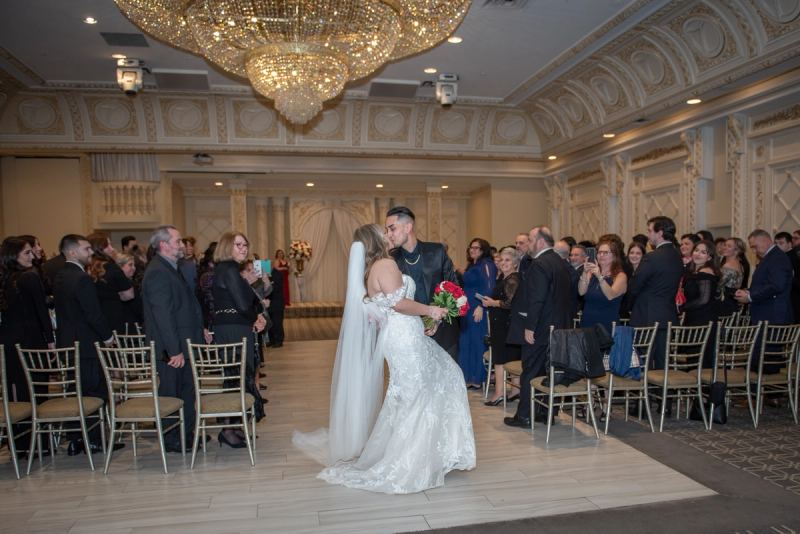 Cassandra and Brandon share a tender kiss at the end of their aisle, surrounded by guests in an opulent ballroom.