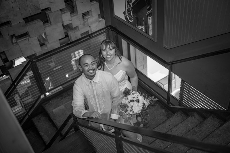 A bride and groom smile from a modern staircase, surrounded by natural light and angular architecture.