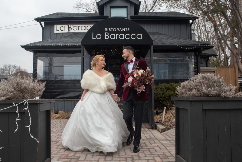 A bride and groom walk hand-in-hand from under an awning, their joy evident in the subdued winter light.